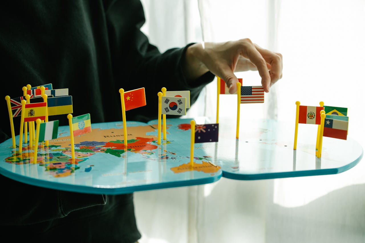 Hand arranging flags on a world map, signifying global diversity.